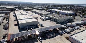 An aerial photo of a carport with solar panels on it. Behind it there is a commercial building, which is a kombucha brewery. This building also has solar panels on the roof. Beside that is a pitched roof building that also has solar panels on much of its 