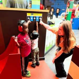 Two children in noise-canceling headphones engage with IBCCES sensory guide, while a staff member assists them.
