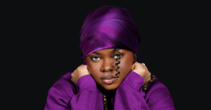 An african-american woman wears a silky purple scarf against a black background.