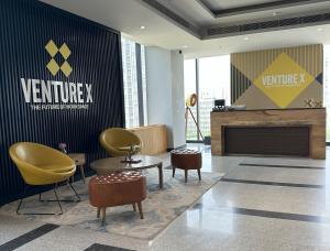 "Modern reception area at Venture X India, Gurgaon, featuring stylish yellow chairs, wooden coffee table, and branded wall signage ‘The Future of Workspace’."