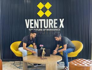 "Two professionals collaborating at Venture X India Gurgaon, seated in modern yellow chairs with a laptop in front of branded workspace wall."