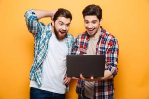 Two excited friends looking at a laptop screen in amazement.