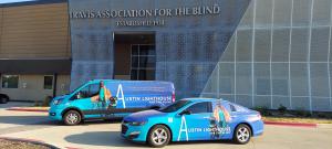 Exterior view of Austin Lighthouse for the Blind building with two bright blue branded vehicles parked in front, showcasing the organization’s logo and mission imagery.