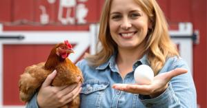 Women holding a chicken and fresh egg with red bard in background.