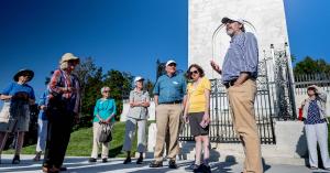 Small group of people in front of a tall monument on a sunny day.
