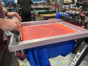Close-up of screen printing process with red ink being applied to a blue t-shirt at Bolt Printing.