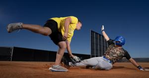 Baseball player in KILOGEAR weighted shorts and shirt sliding into home plate during a game, with a catcher in full gear wearing KILOGEAR apparel attempting to tag him out.