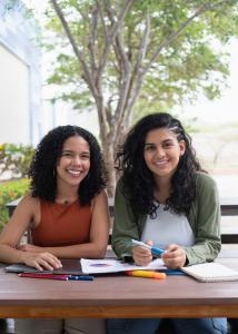 Two smiling Latina college students sitting together, representing the diverse student population served by Equilibrium Mental Health