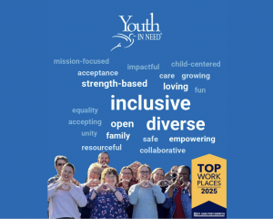 A group of smiling Youth In Need staff stand together making heart shapes with their hands in front of a blue background filled with words like “inclusive,” “diverse,” and “empowering,” alongside a 2025 Top Workplaces badge.