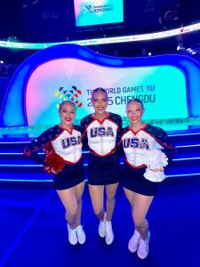 3 athletes in uniform with poms on the stage for the world games