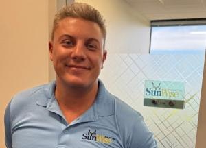 Chris Murray, Director of Equipment Financing at Sunwise Capital, smiling in a Sunwise-branded polo shirt, standing in front of his new office with a Sunwise Capital sign on the glass wall.