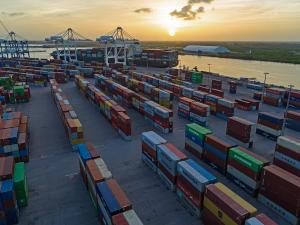 Shipping containers stacked in a large port yard along a coastal canal.