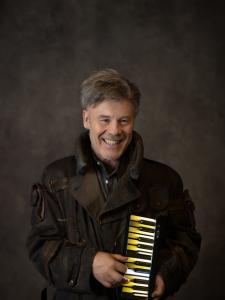 Thomas Dolby in trench coat grinning with mini keyboard