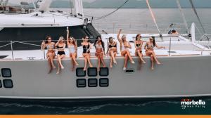 A group of women celebrating a Marbella hen party on a luxury catamaran, wearing swimsuits, holding drinks and enjoying the Mediterranean view.