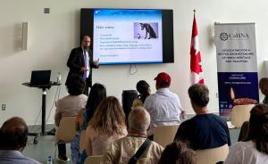 Marc Bellerose of Montreal Police Hate Crimes Unit speaks to a seated audience at CoHNA’s Suraksha workshop on combatting Hinduphobia. A Canadian flag and CoHNA banner are placed beside him.