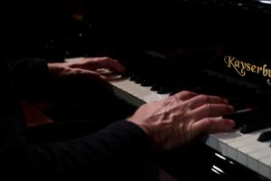 warm piano keyboard image with a man's hands playing the piano in a darkened studio