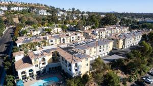 An apartment complex on a hillside in San Diego has solar panels visible on various parts of the tile roofs.