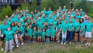 Large multigenerational group wearing matching teal custom t-shirts at an outdoor gathering.