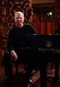 Ed Bazel, tall with white hair, dressed in black, sits at the piano in a darkened recording studio at Skywalker Sound