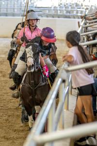 young girl safely watches polo players charging up the rail at a polo competition