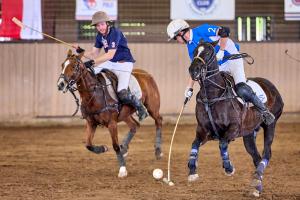 male polo players shoulder for a shot on the ball on horseback during polo game