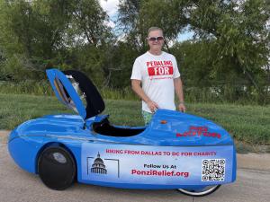 Man standing next to a blue human-powered velomobile with 'No Motor' signage, promoting a charity bike ride from Dallas to Washington, D.C. to support the Stargrower Family through PonziRelief.org