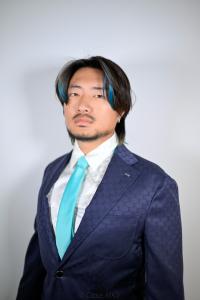 Kai Zhang, founder of Secret World, standing in a studio portrait with a navy patterned suit and turquoise tie, looking confidently into the camera.