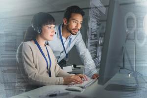A man and a woman work on a computer. There is a transparent overlay of computer system screens.