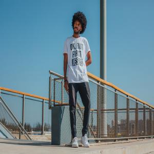 A young African American man wearing a white t-shirt and jeans in an industrial setting