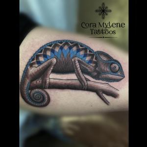 Chameleon tattoo with blue geometric scales and bold outlines on arm, designed by Austin tattoo artist Cora Mylene.