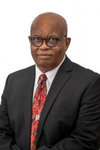 Image of the top half of a man in glasses wearing a suit and tie looking at the camera.