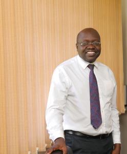 Image of the top half of a man in glasses wearing a shirt and tie smiling at the camera.