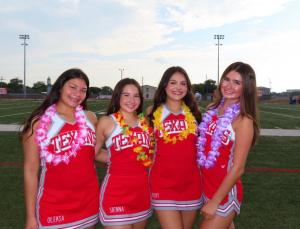 Image of four Ray High School cheerleaders wearing their red and white "Texans" uniforms. All four girls are also wearing Hawaiian inspired lei's around their necks.