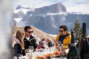 Restaurant terrace in the Dolomites with gourmet food, wine, and views of the Sella mountain range and Marmolada – ski holiday Dolomites, ski deals Dolomites, Val Gardena ski holiday, Dolomites ski packages.