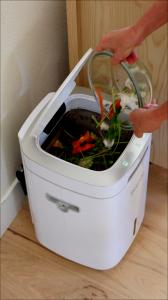 "Hands emptying food scraps from glass bowl into open white Reencle home composter showing decomposing organic matter inside"