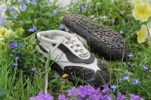 “Biological Footprint" by Evelina Lavergren, winner of the Footwear category. A pair of sustainable white sneakers with black detailing lies in grass among wildflowers. The shoes are made from biomaterial derived from seaweed, designed to disperse seeds a