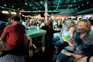 A crowd of people watch songwriters at a nighttime venue