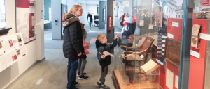 A family explores a museum exhibit featuring historical artifacts, a wooden chair, and informative displays about voting history.