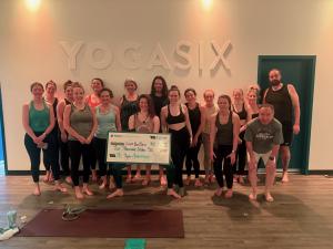 Group of YogaSix South Hills team members standing together with a large ceremonial check, marking over $27,000 donated since 2021 to LoveYourBrain, a nonprofit supporting people affected by traumatic brain injury.