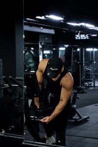 Man wearing a GYM NYC cap and tank top adjusts strength equipment inside the Lexington flagship gym, highlighting the facility’s performance-focused training atmosphere.