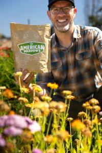 Ryan Heck, smiling American Meadows customer in Oregon, standing beside vibrant wildflower blooms and holding a bag of premium wildflower seeds, highlighting successful meadowscaping results.