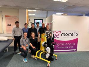 Group photo of RoboCT and Morrello Clinic teams standing beside a RoboCT exoskeleton at the clinic, smiling after training and celebrating their UK collaboration.