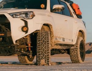 A white Toyota 4Runner equipped with Ride Shocks suspension kicks up mud as it powers through rugged off-road terrain at sunset.