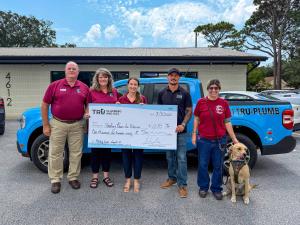 Healing Paws for Warriors representatives Dennis Krebs, Chris Krebs, Sam Hay, Monika Baltazar, and her service dog Buddy pose with Cody Kearns, owner of Tru Plumbing and Gas pose with a giant check made out to Healing Paws for Warriors in the amount of $1
