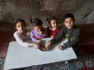 Sewar, Mayar, Lamar, and Aboud, 4 children in Gaza, sit together on the floor eating a shared snack