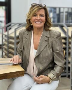 A woman with a brown jacket and white pants sits at a table.