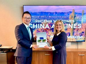 China Airlines President Kevin Chen and Phoenix Mayor Kate Gallego smile while holding a folder together, with a screen behind them reading “Phoenix Welcomes China Airlines” against a desert skyline.