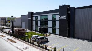 Exterior view of Simsek Makina Takim factory with glass and black facade, front garden, and parking area