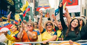 Group of people waving Ecuadorian flags and colorful fans in Times Square, smiling and cheering as part of the “Latinos in Times Square” Hispanic Heritage Month event.