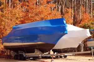 Boat under protective winter cover with fall leaves, illustrating proper boat winterization before freezing temperatures.